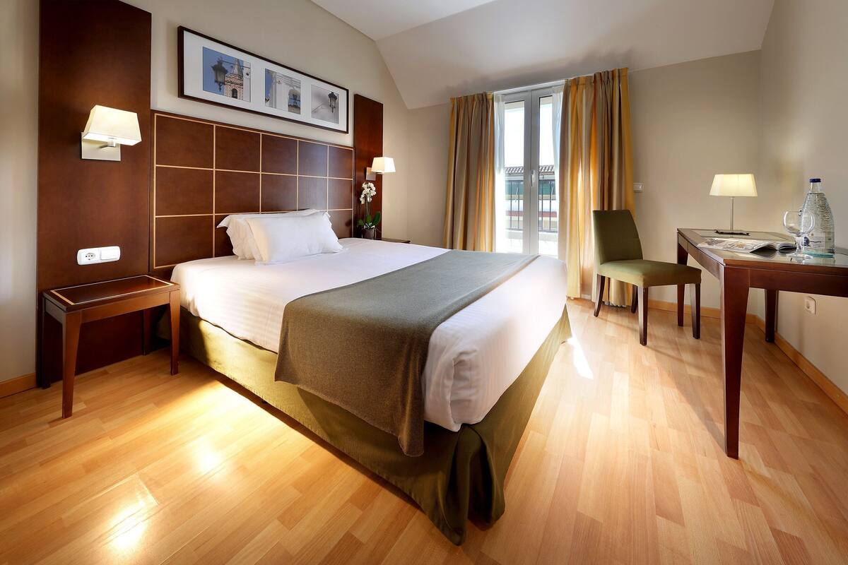 Une chambre d’hôtel avec un grand lit, un bureau, une chaise et une fenêtre avec des rideaux.