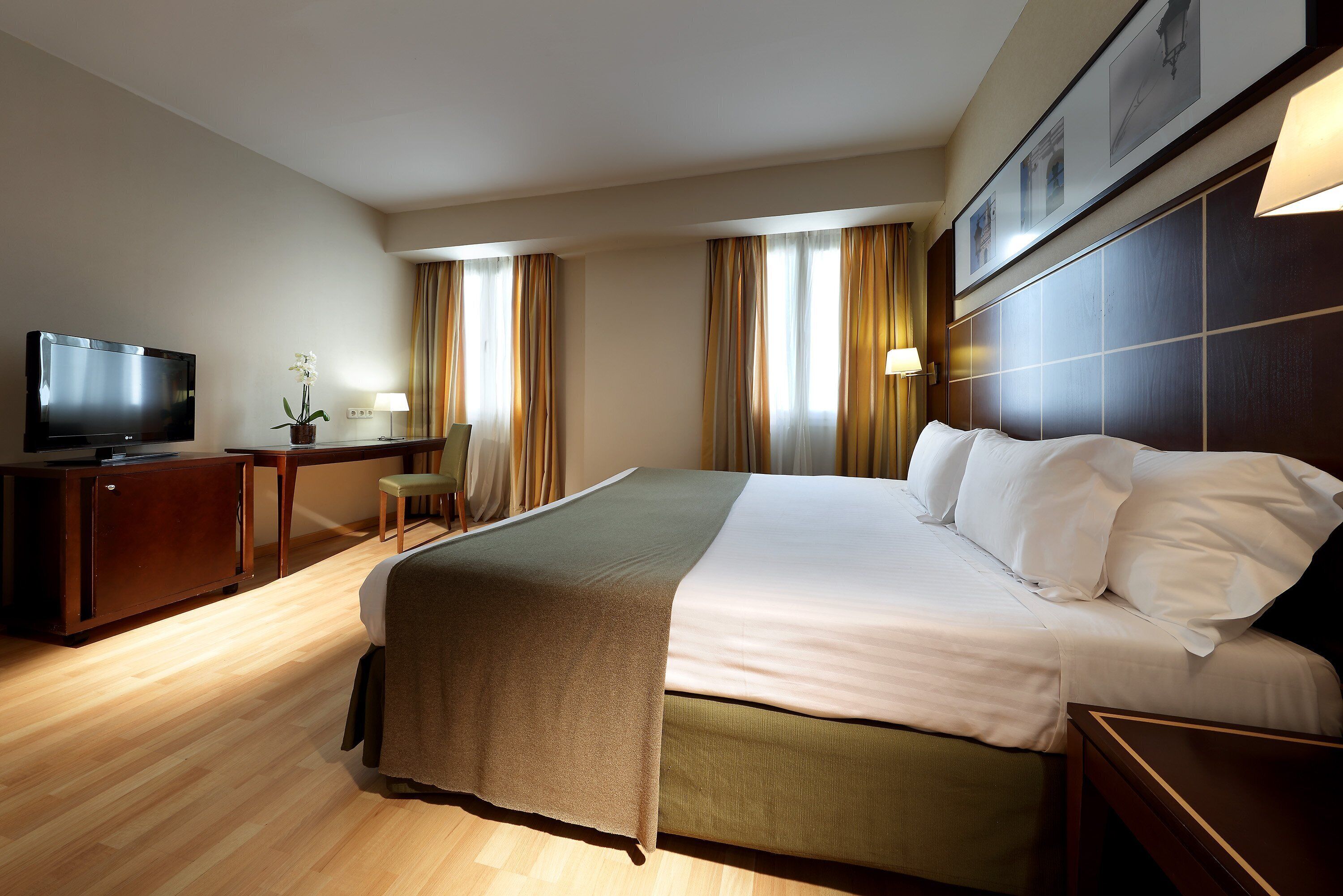 Una habitación de hotel con una cama grande, un escritorio con televisor y una silla.