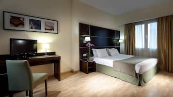 Een hotelkamer met een bed, bureau, stoel, televisie en kunst aan de muur.