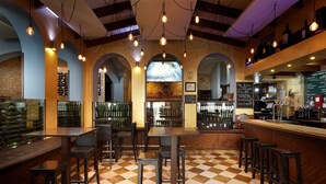 A bar area with checkered flooring, wooden bar stools, and hanging pendant lights. - Hotel Dorma Tartessos (Huelva)