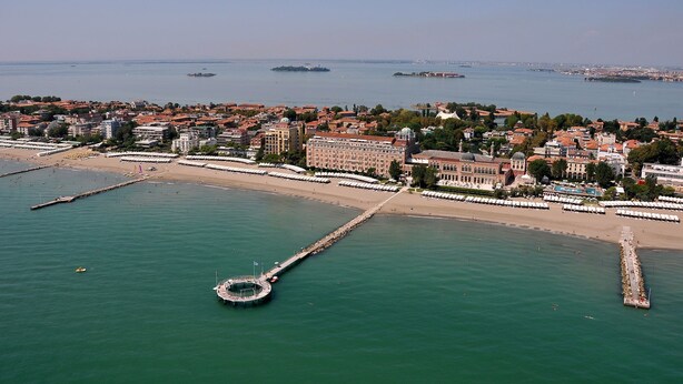 Vista aérea de una ciudad costera con un paseo marítimo destacado, un gran hotel de arquitectura clásica y una estructura portuaria circular.