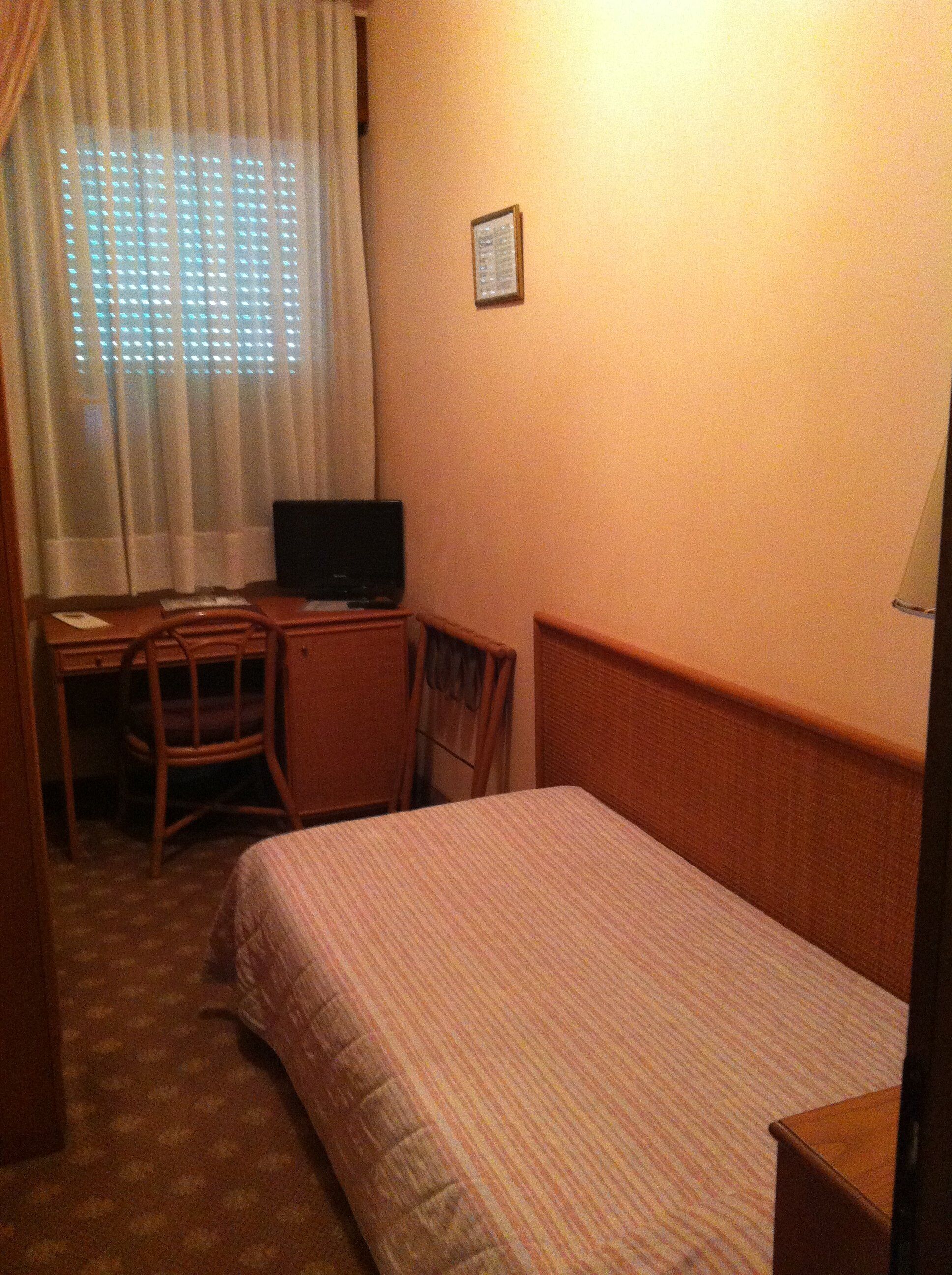A hotel room with a bed, a desk, a chair, and a television.