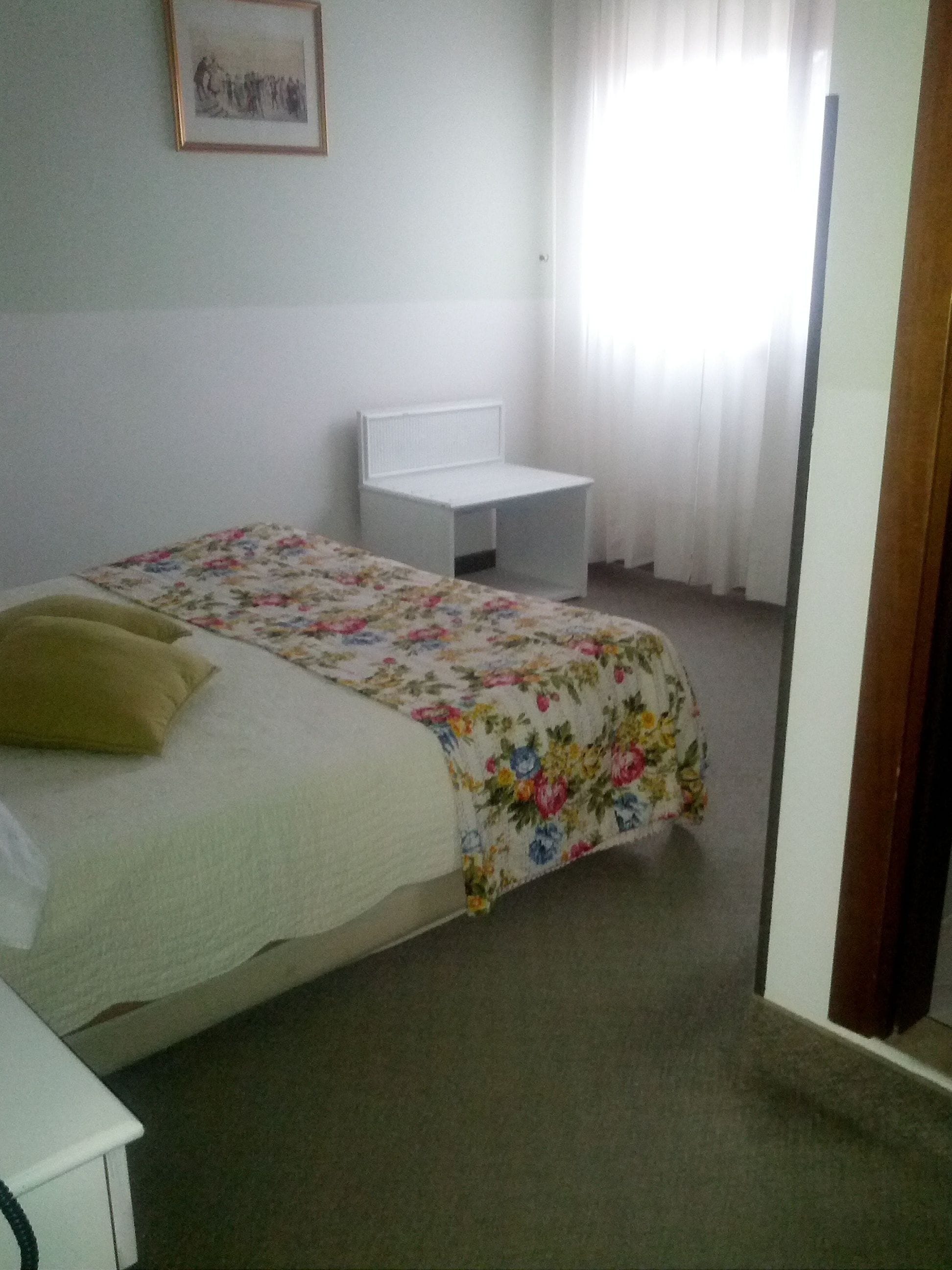 A bedroom with a bed, a bedside table, a chair, and a window with curtains.