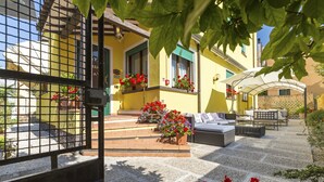 Un patio con mobiliario exterior, plantas en macetas y una entrada con reja.