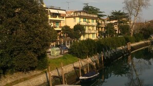 Un canal con barcos amarrados, una hilera de edificios con balcones y árboles a lo largo de la orilla.
