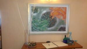 Un cuadro abstracto enmarcado en una pared sobre un escritorio de madera con un cuaderno, un bolígrafo y una pequeña escultura.