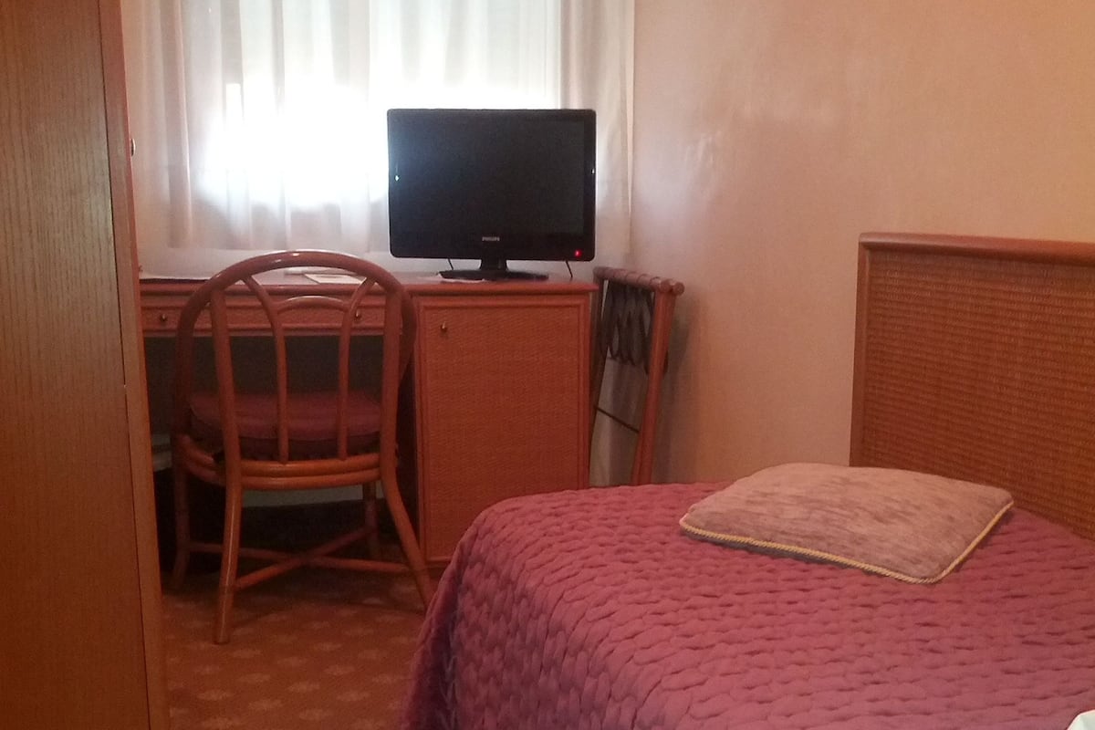 A hotel room with a bed, a desk with a computer, and a chair.