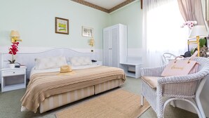Un dormitorio ordenado con cama, mesitas de noche, una silla de mimbre y un armario.
