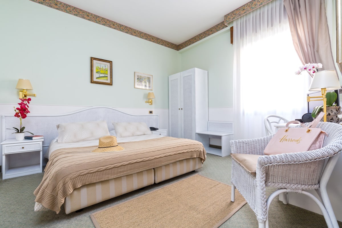 A neatly arranged bedroom with a bed, bedside tables, a wicker chair, and a wardrobe.
