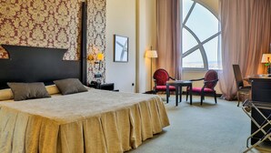 A hotel room with a large bed, a desk with a chair, a window with curtains, and a patterned wallpaper. - Hotel Velada Mérida (Merida)