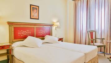 A hotel room with a large bed, a nightstand, a lamp, a chair, and a curtain.