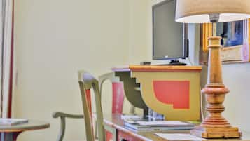 A room with a desk, chair, lamp, and a television on the wall.