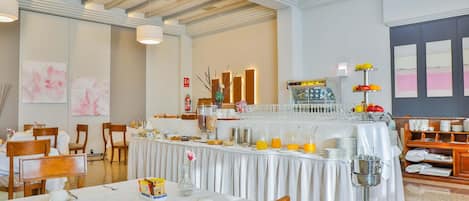 Une salle à manger d’hôtel avec des tables préparées pour le petit-déjeuner, un buffet proposant divers plats et un coin café.