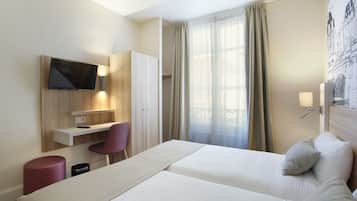 Une chambre d’hôtel avec un lit, un bureau et une chaise, une télévision et une fenêtre avec des rideaux.