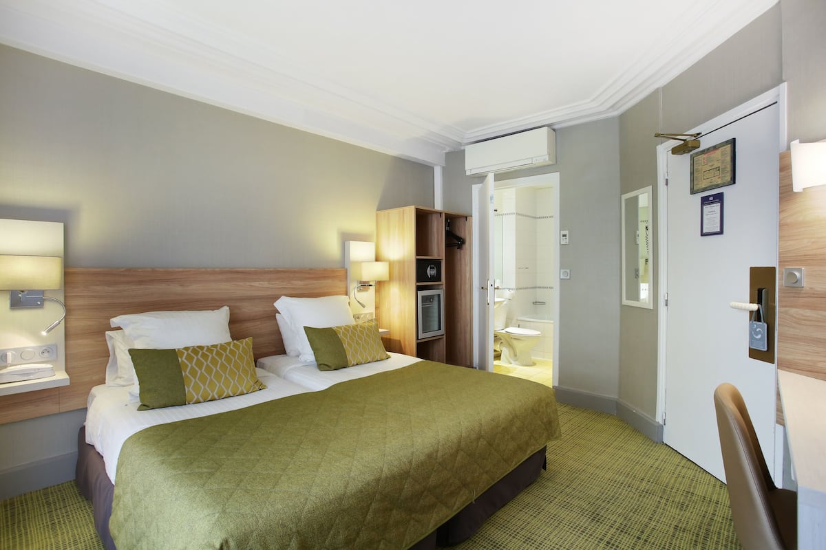 A hotel room with a large bed, bedside tables, a wardrobe, and a bathroom visible through an open door.