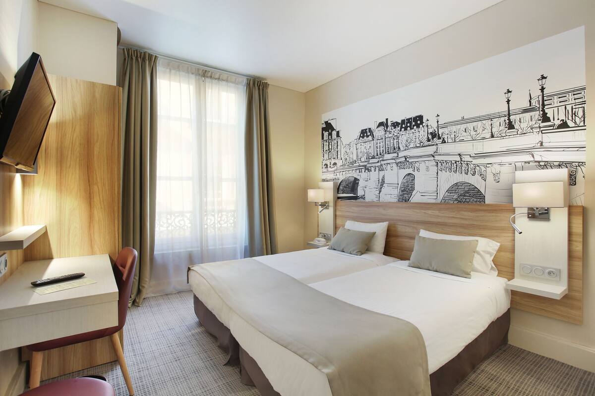 A hotel room with a large bed, a desk with a chair, a TV, and a wall mural.