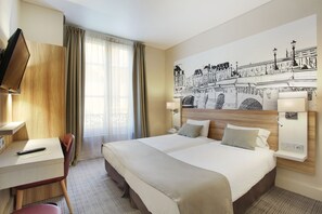 A hotel room with a large bed, a desk with a chair, a TV, and a wall mural.