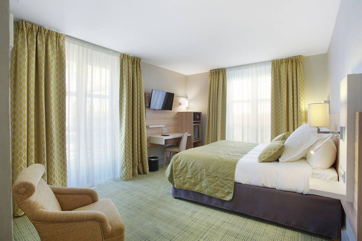 A hotel room with a bed, a desk, a chair, and a television.