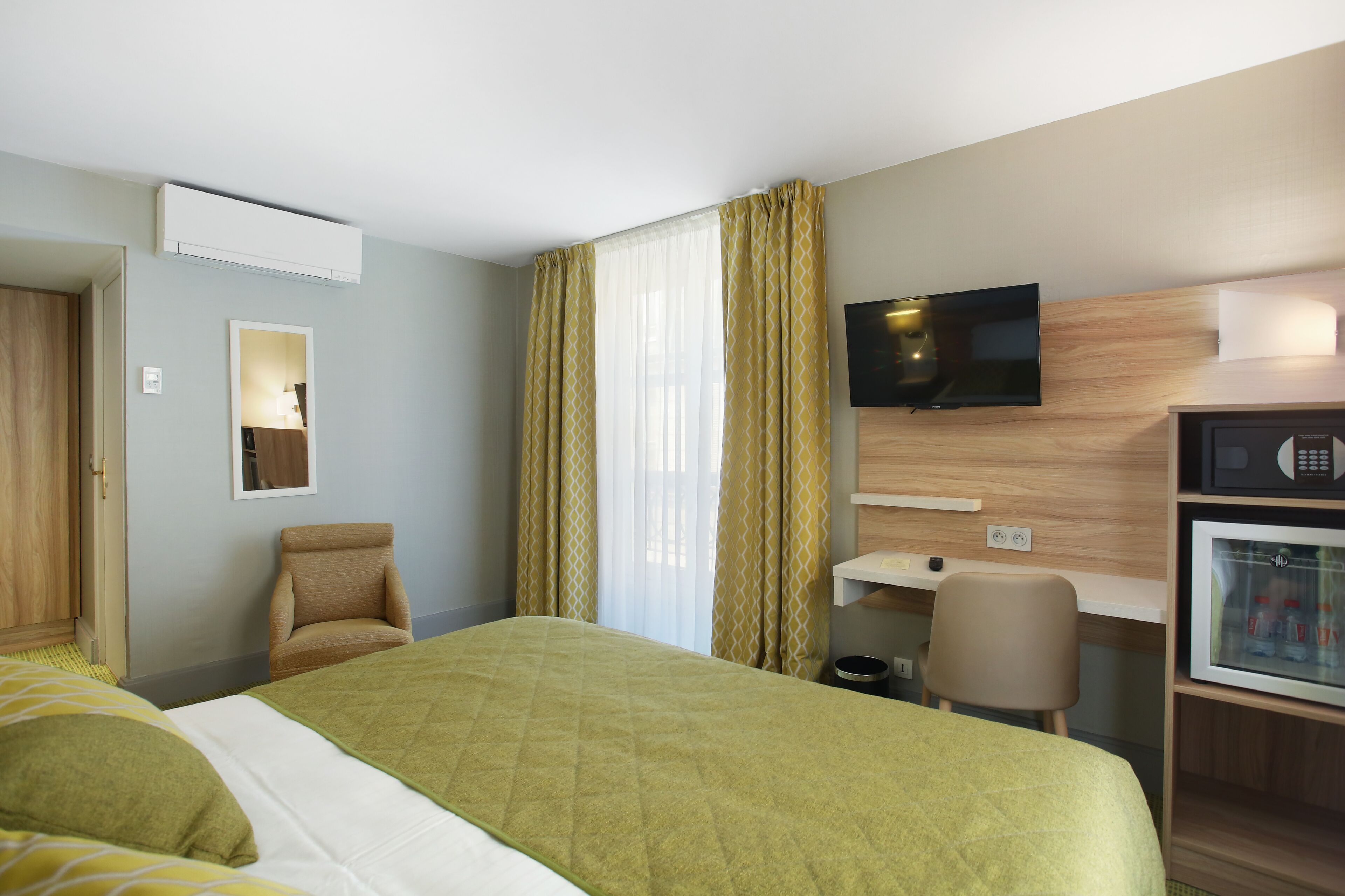 A hotel room with a bed, a chair, a desk, a television, and a minibar.