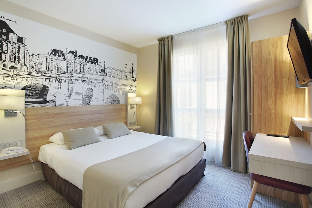 A hotel room with a large bed, a desk, a flat-screen TV, and a wall mural of a cityscape.