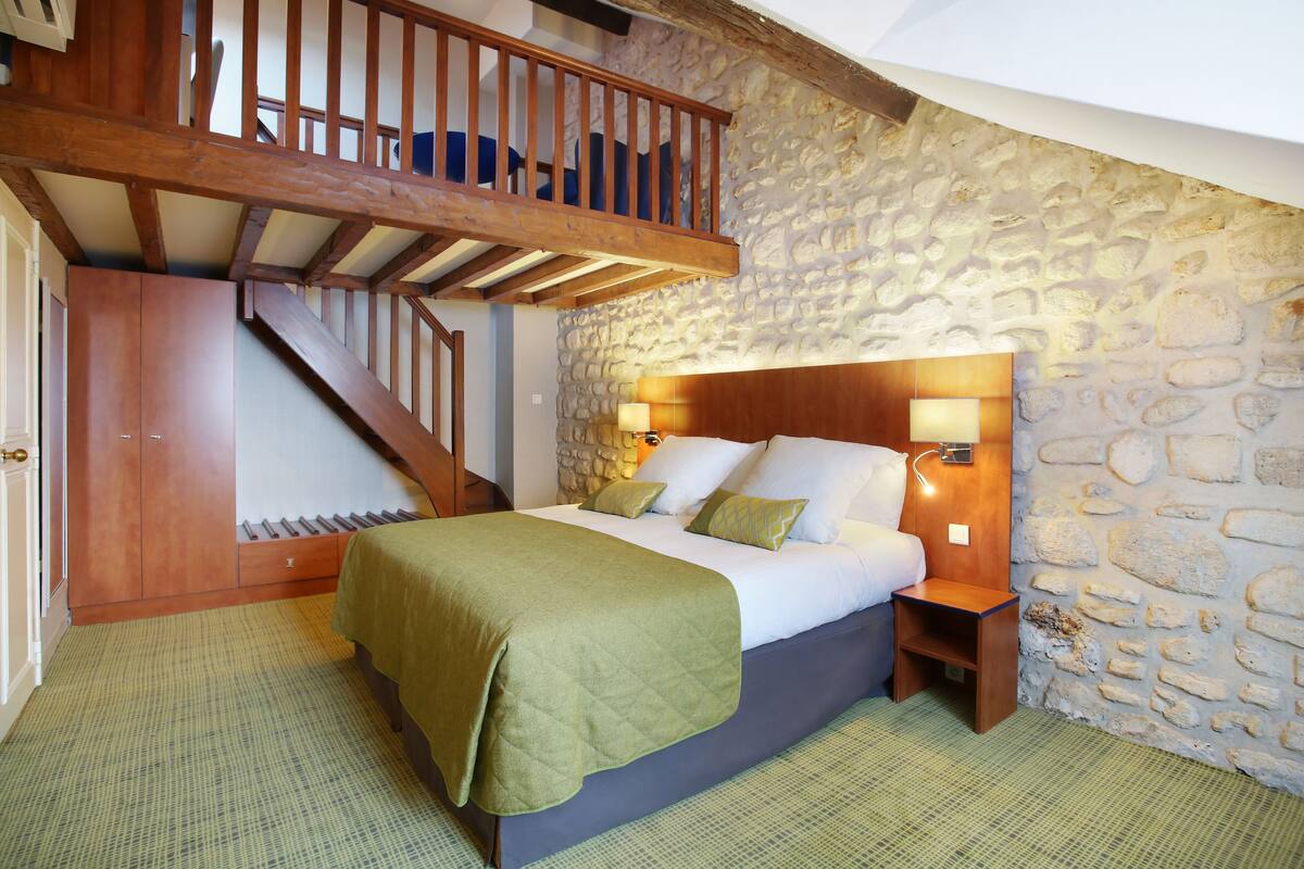 A bedroom with a stone wall, wooden staircase, and a bed with green bedding.