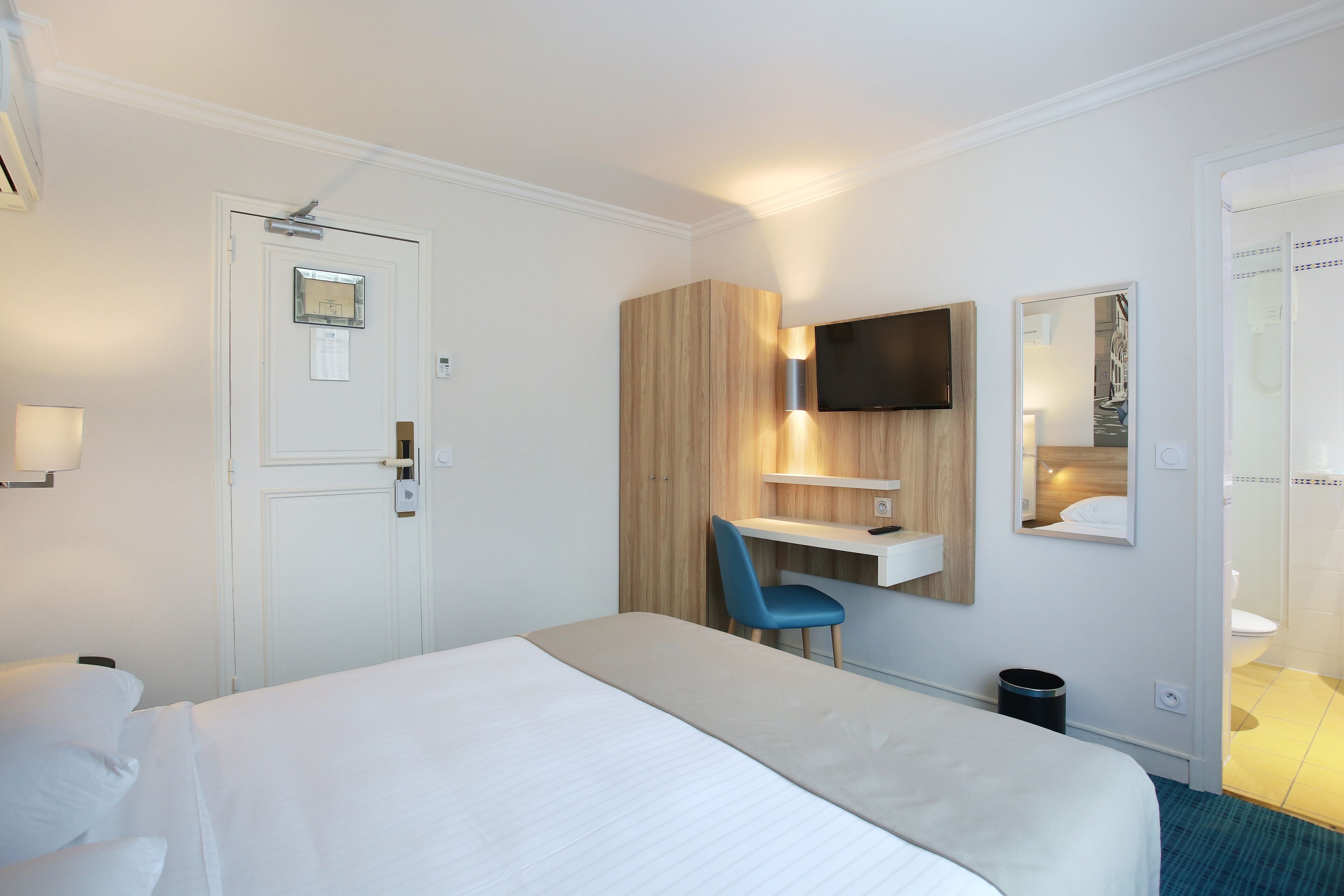 A hotel room with a bed, a desk, a chair, a TV, and a bathroom.