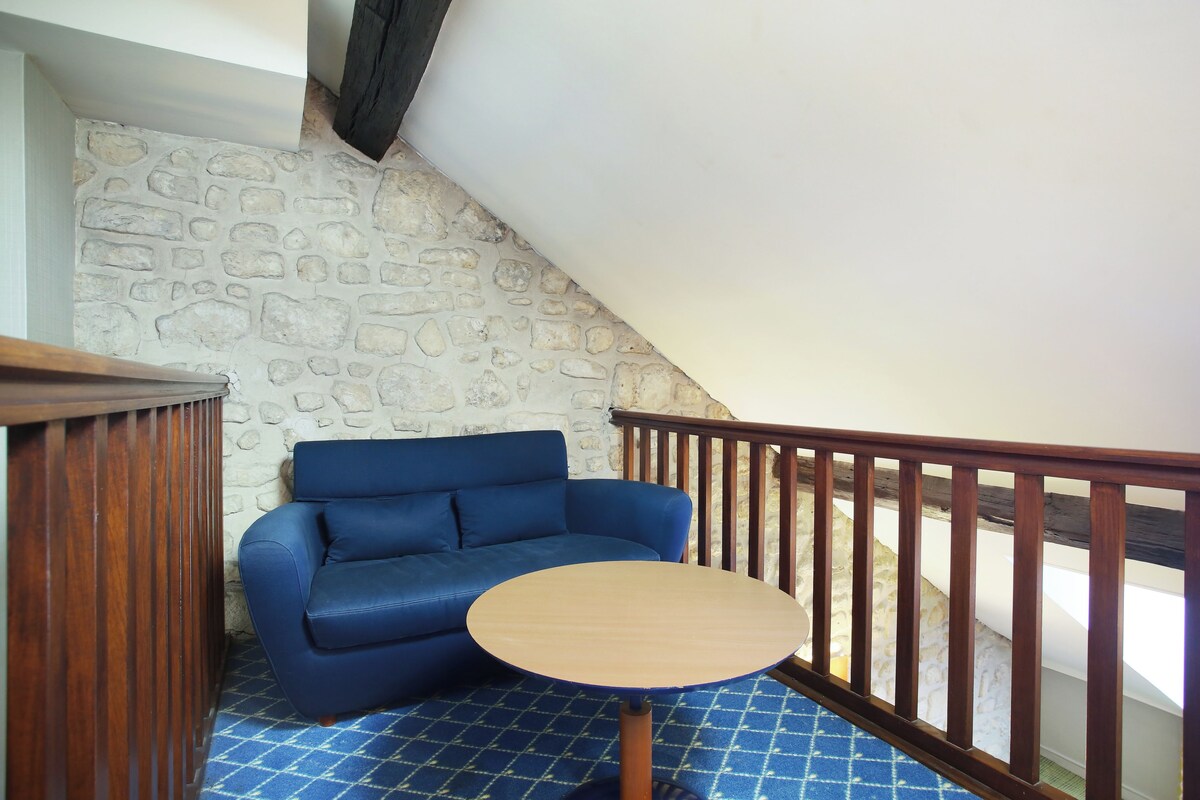 A blue sofa and a small wooden table in a corner with a stone wall and wooden railing.