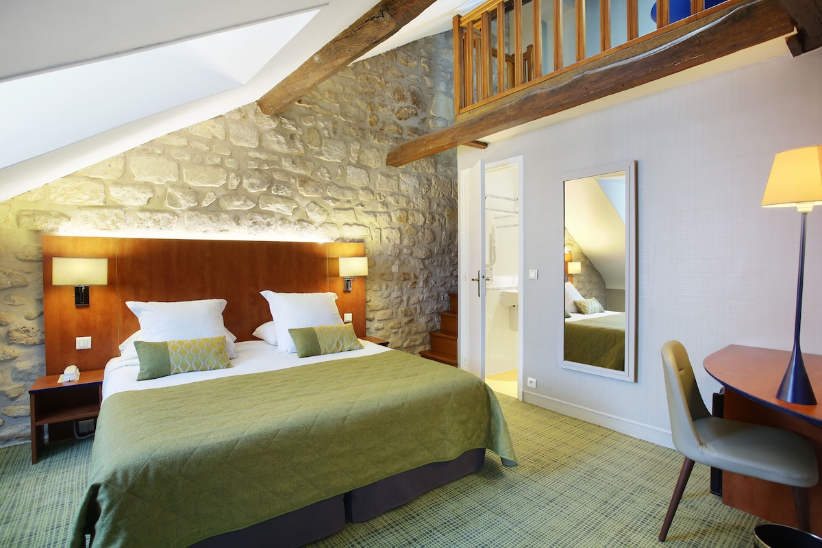 Ein Schlafzimmer mit Steinwand, hölzernem Kopfteil, einem Bett mit grüner Bettwäsche, einem Nachttisch, einem Schreibtisch mit Lampe und einem Spiegel.