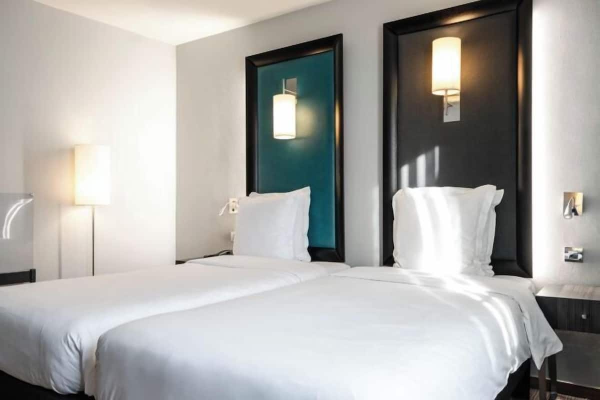 Une chambre d’hôtel avec un grand lit, deux tables de chevet, une petite table et deux lampes fixées au mur.