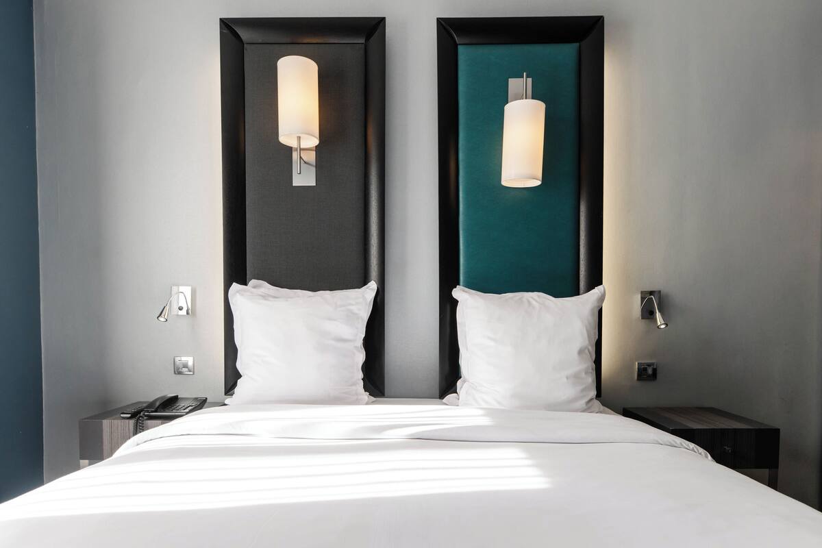 Une chambre d’hôtel avec un grand lit, deux tables de chevet, un téléphone et des luminaires fixés au mur.