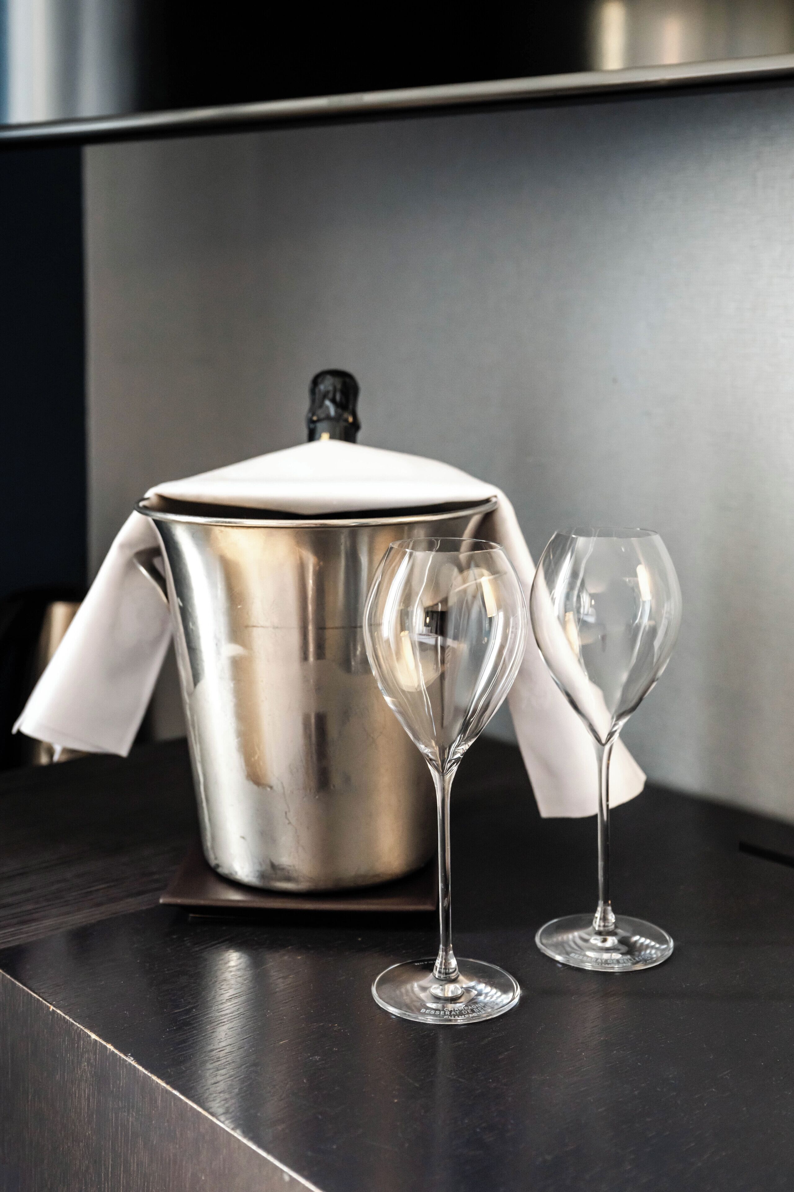 Une casserole en acier inoxydable avec un couvercle, posée sur une surface sombre, accompagnée de deux verres à vin vides.