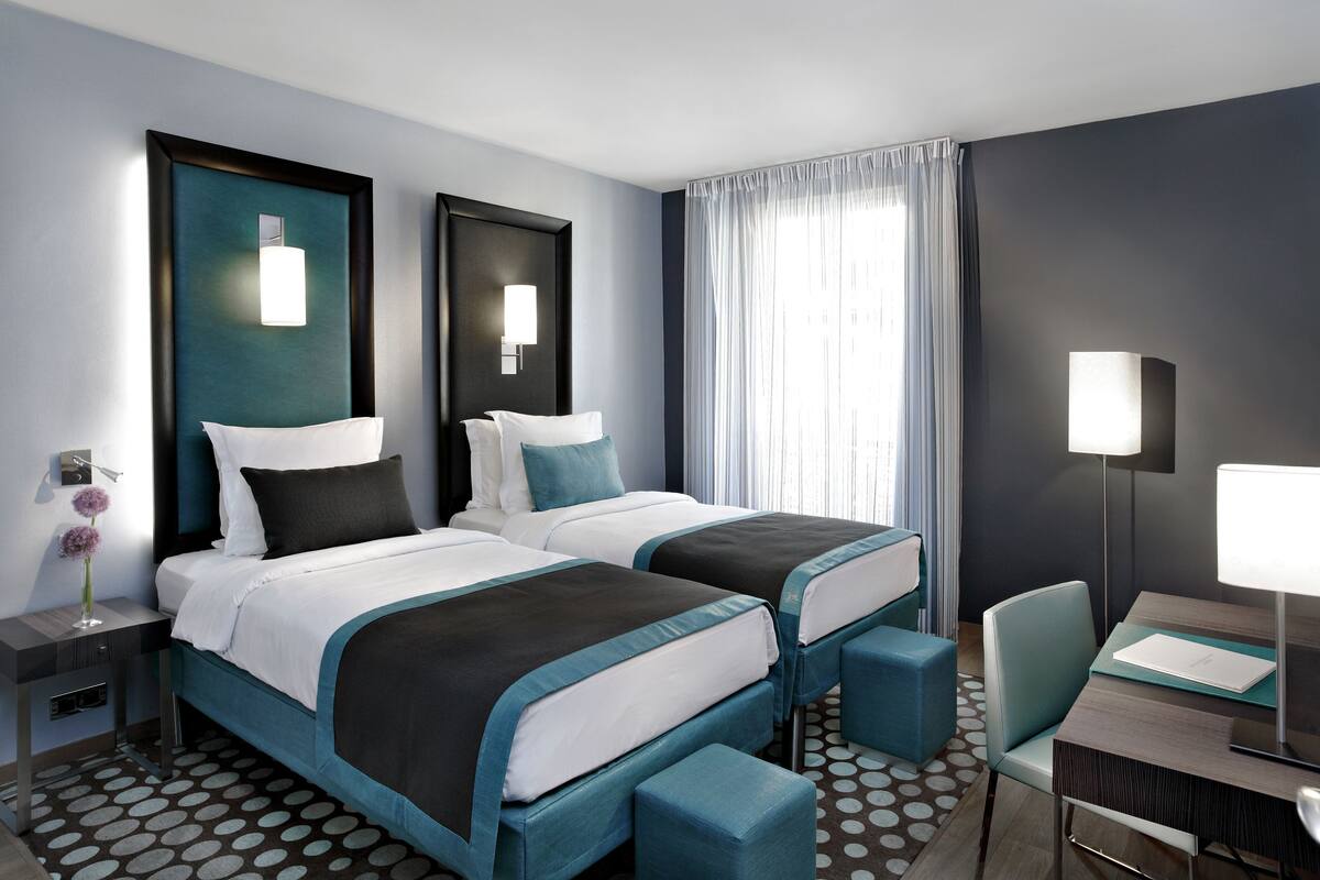 Une chambre d’hôtel avec deux lits, un bureau, une chaise, une table de chevet et une lampe.