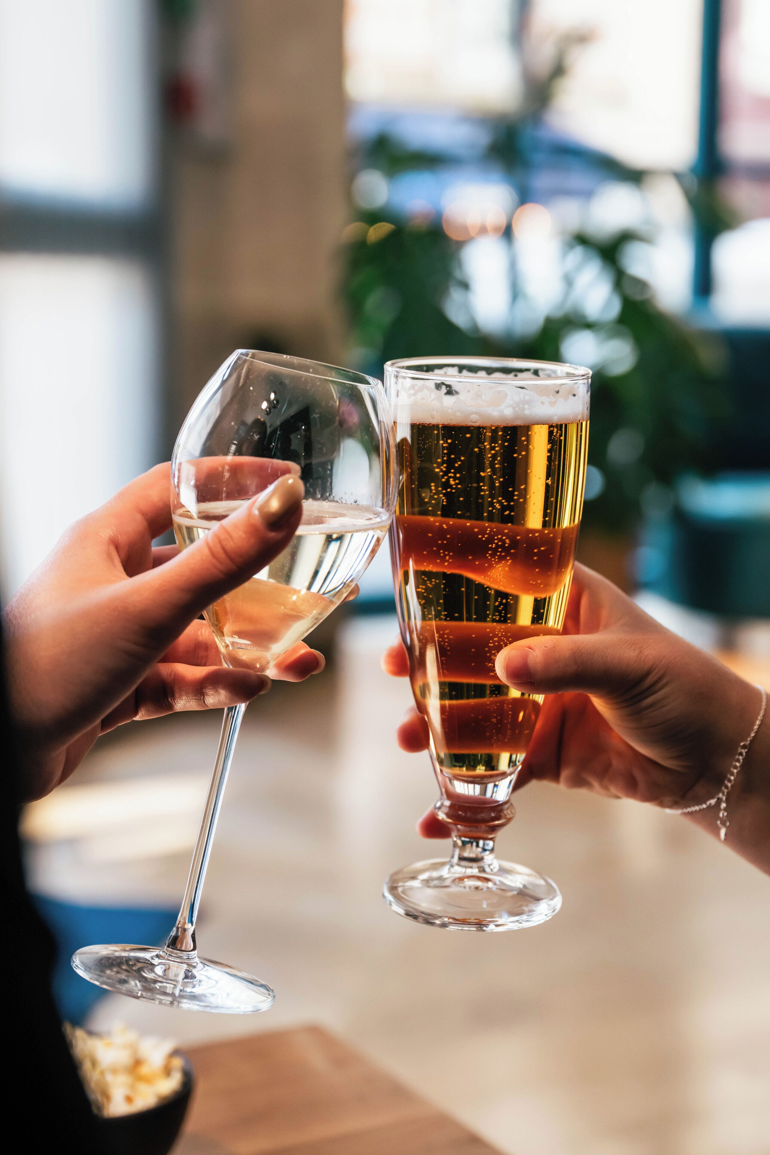 Two hands holding glasses of beer, one with a stemmed glass and the other with a tulip glass, in a setting with a blurred background.