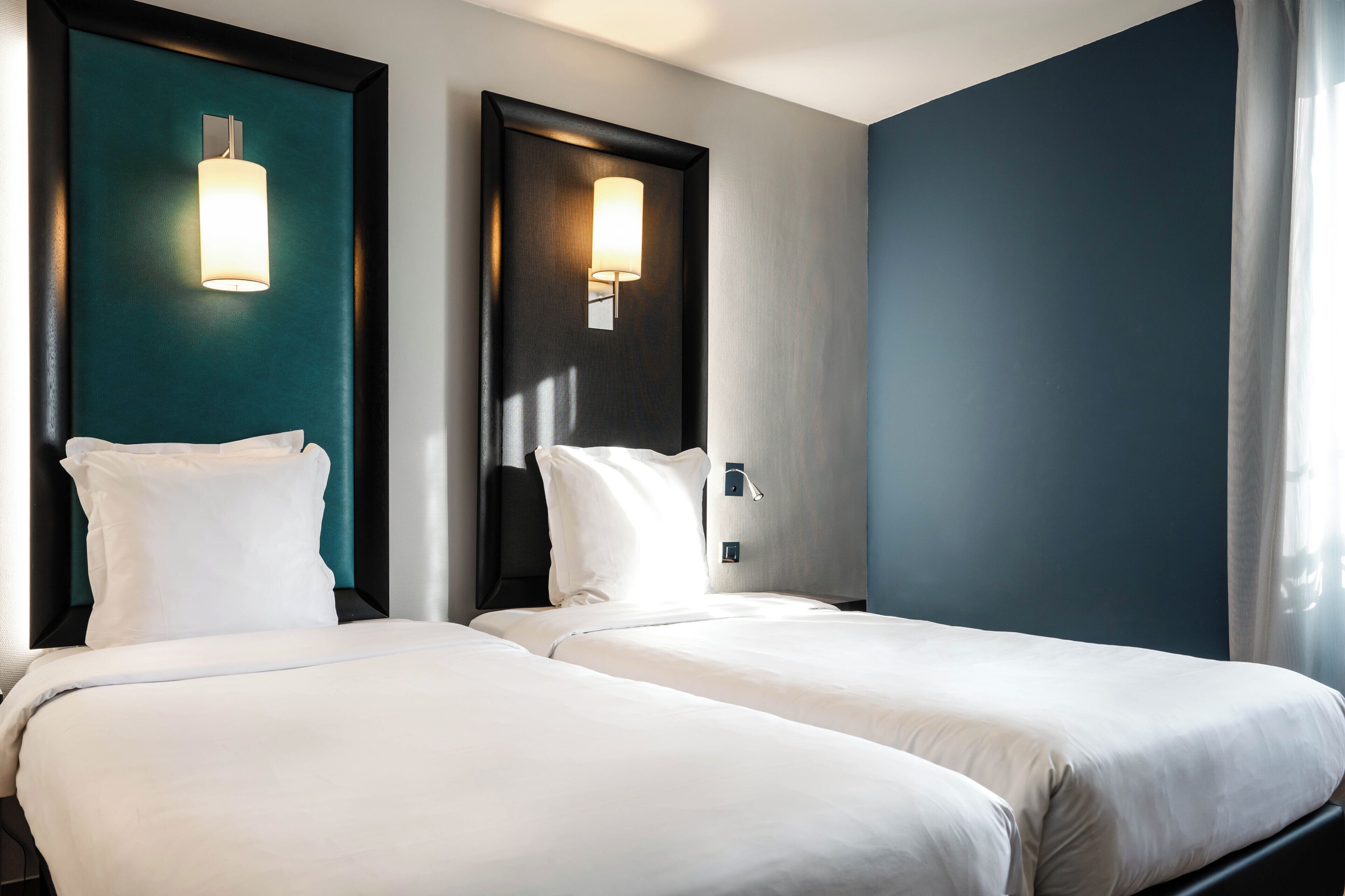 Une chambre d’hôtel avec deux lits, une tête de lit de couleur foncée et un mur d’accent de couleur turquoise.
