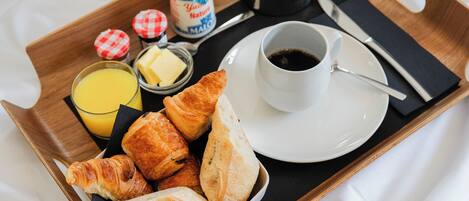 A tray with croissants, a coffee pot, a cup of coffee, a glass of orange juice, and a container of butter.