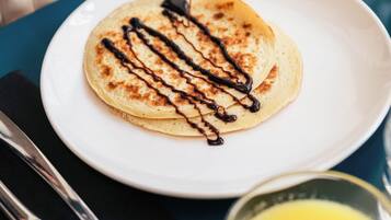 Un plato de tortitas con jarabe, un tenedor, un cuchillo y un vaso de zumo de naranja sobre una mesa.
