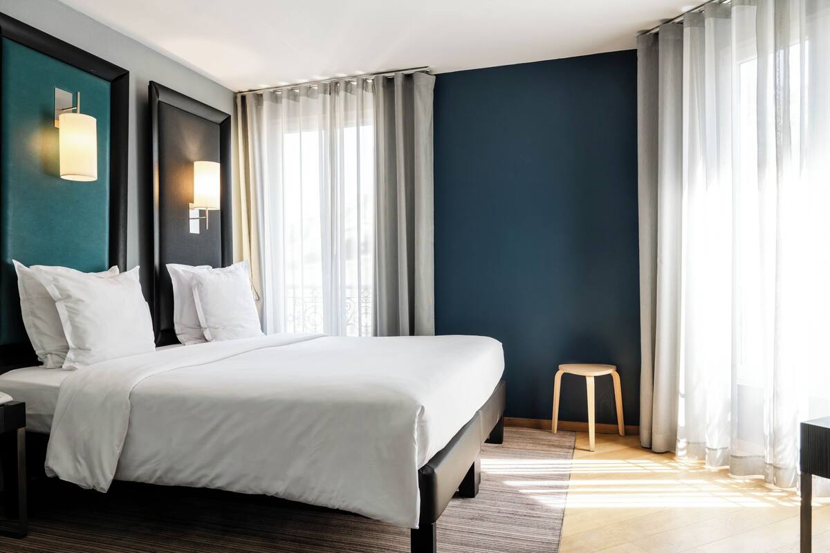 Une chambre d’hôtel avec un lit, une table de chevet, une chaise et une fenêtre avec des rideaux.
