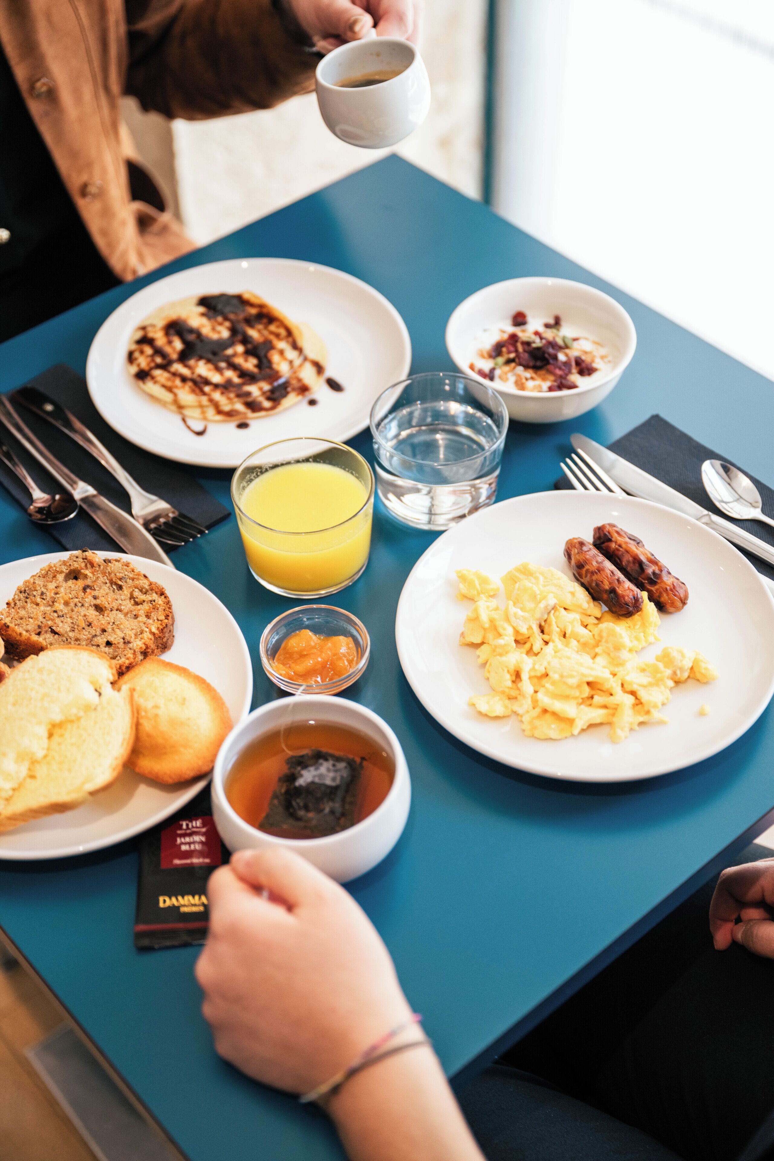 A breakfast table with plates of food, a glass of orange juice, and a cup of coffee.