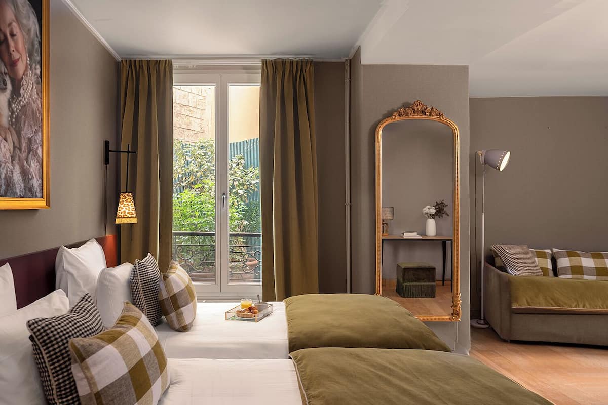 A hotel room with a bed, a sofa, a mirror, and a view of the outdoors.