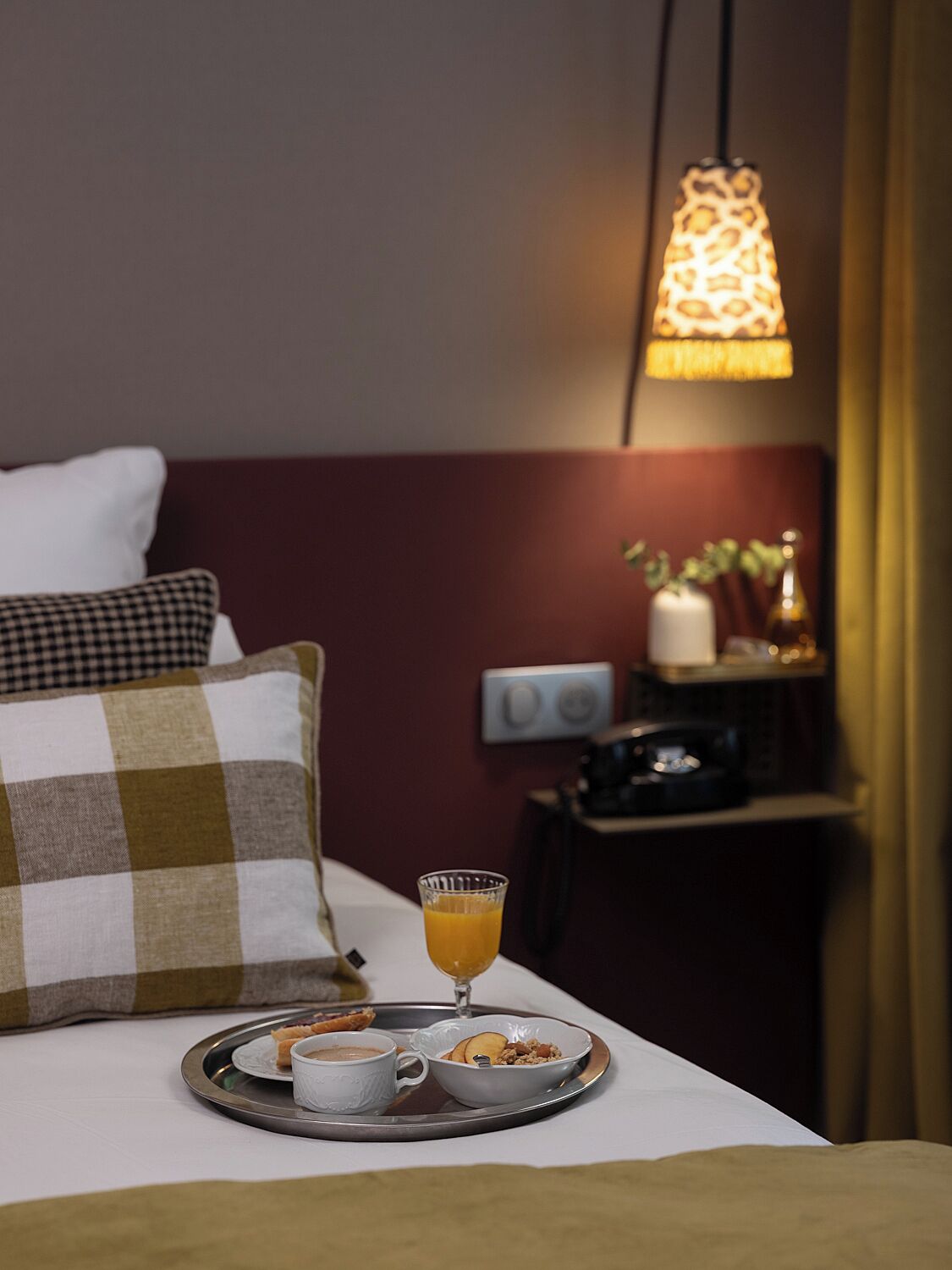 A neatly made breakfast tray with a cup of coffee, a glass of orange juice, and a plate of food on a bed.