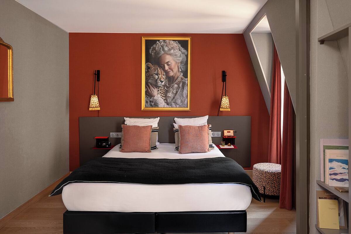 A bedroom with a large bed, two bedside tables, a wall-mounted picture, and a window with curtains.