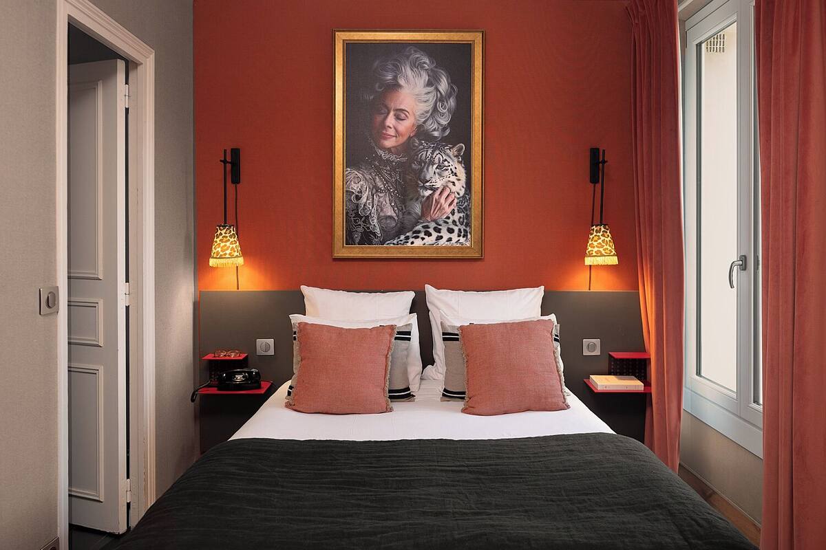 A hotel room with a large bed, two nightstands, a painting on the wall, and a window with curtains.