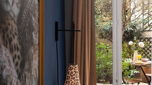 A room with a large window, a leopard print lamp, and a view of a garden with a table and chairs outside. - Hotel Zélie Champs-Elysées (Paris)