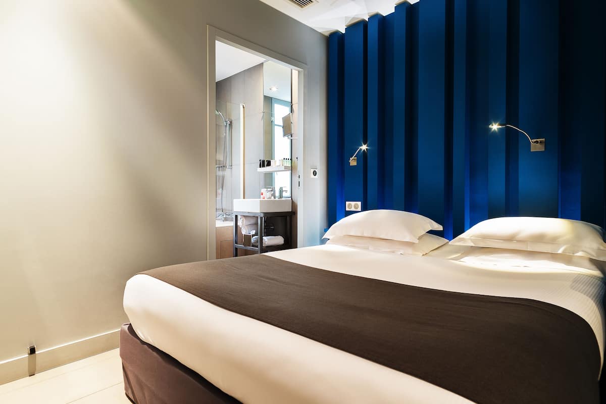 Habitación de hotel con una cama grande, baño con espejo y pared azul de acento.