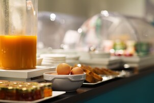 Un buffet per la colazione con un contenitore di vetro pieno di succo d'arancia, una ciotola di uova e diversi pasticcini.