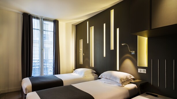 A hotel room with two beds, a bedside table, a nightstand, a wall-mounted TV, and a window with curtains. - Hotel Arc de Triomphe Etoile (Paris)