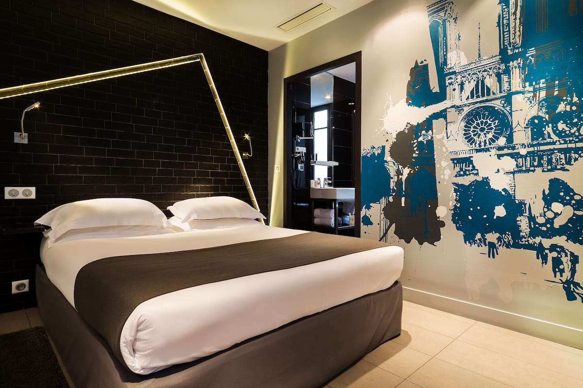 Habitación de hotel moderna con una cama grande, una pared de ladrillo negro y un mural de un paisaje urbano.