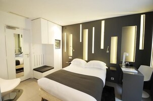 Habitación de hotel moderna con una cama grande, un escritorio y una silla. Se observa un armario y un espejo en la pared.