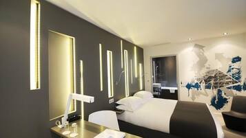 Camera d'albergo moderna con un letto, comodino e una scrivania con una sedia. Si nota anche un grande specchio e delle opere d'arte a parete.