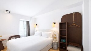 Une chambre d’hôtel avec un grand lit, une table de chevet, une lampe, une armoire et un petit tabouret rond.